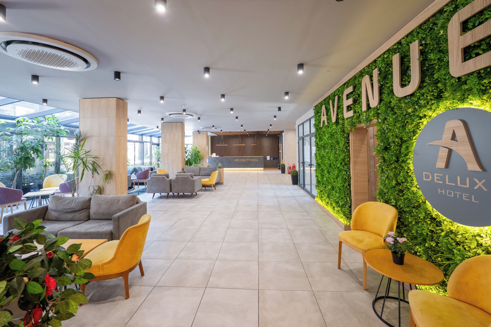 Vestíbulo de hotel con mostrador de recepción, zona de estar y una pared decorada con plantas y el nombre del hotel.