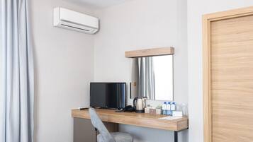 A hotel room with a wooden desk, a television, a chair, a mirror, and an air conditioning unit.
