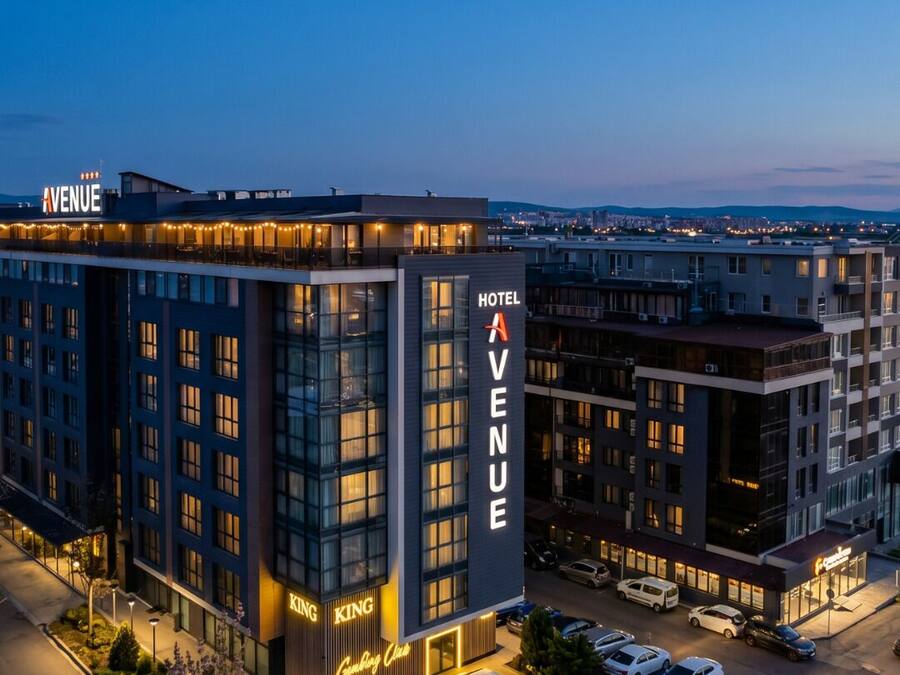 Un hotel llamado 'Avenue' con un diseño moderno, que cuenta con un llamativo letrero vertical y una fachada bien iluminada.