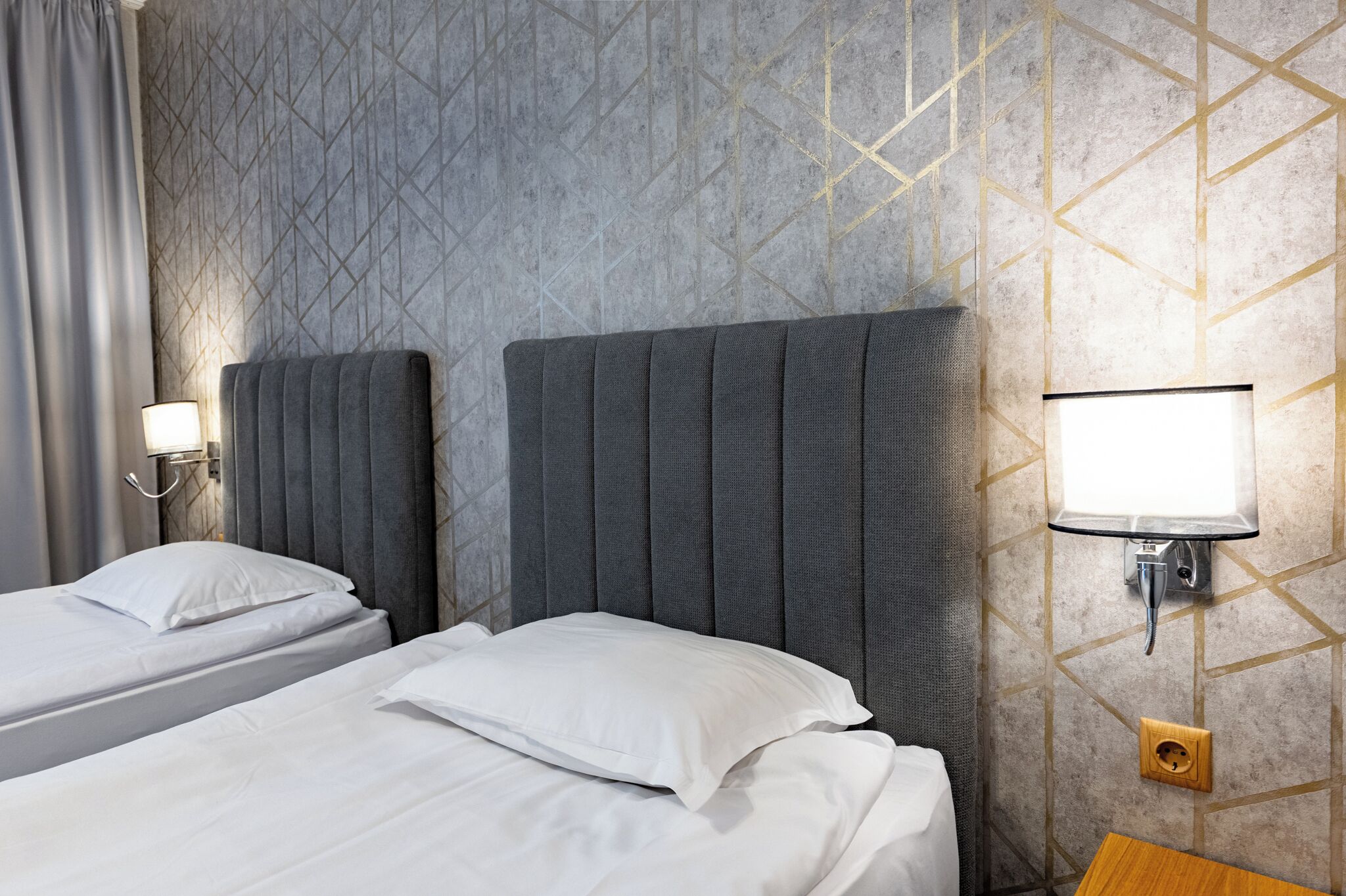 Habitació d'hotel amb dos llits, una tauleta de nit, una làmpada penjada a la paret i una presa elèctrica.