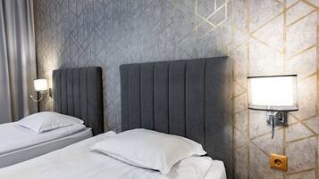 Habitació d'hotel amb dos llits, una tauleta de nit, una làmpada penjada a la paret i una presa elèctrica.