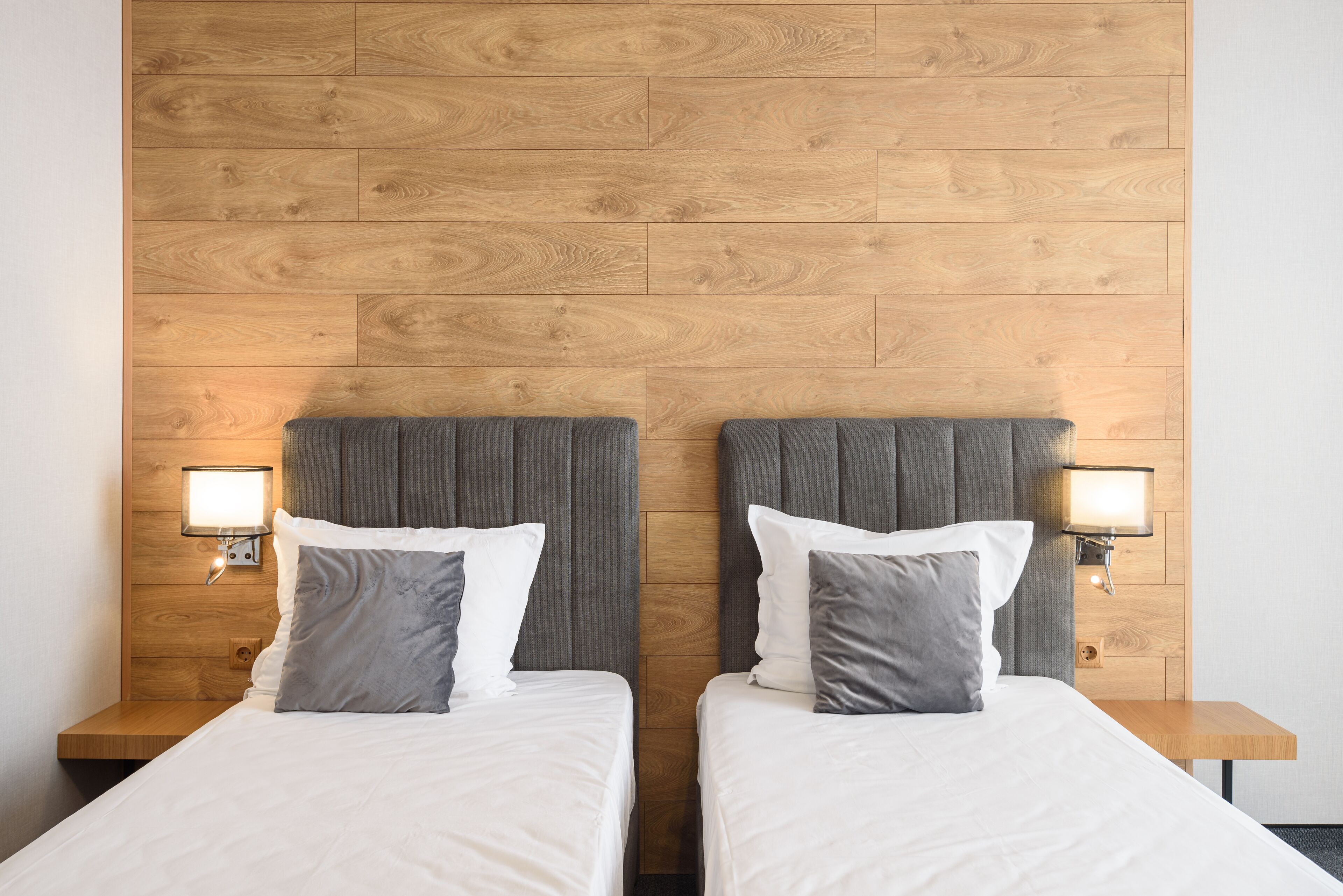 Een hotelkamer met twee bedden, houten hoofdeinden en bedlampjes.