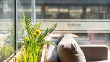 A window with a view of a building labeled "BUNYA" and a wooden planter with green plants and yellow flowers.