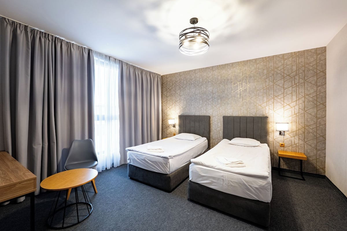 A hotel room with two single beds, a wooden table, a chair, and a desk.