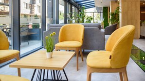 Un área de estar interior moderna con sillas amarillas y grises, una mesa de madera y una planta en maceta.
