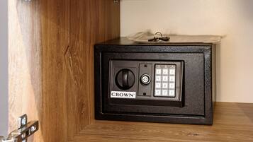 Una caja fuerte con teclado y cerradura de combinación, identificada con la etiqueta “CROWN”, ubicada debajo de un estante de madera.