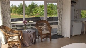 Un dormitorio con cama, dos sillones de mimbre, una mesita redonda con un florero y vistas a la vegetación a través de amplios ventanales.