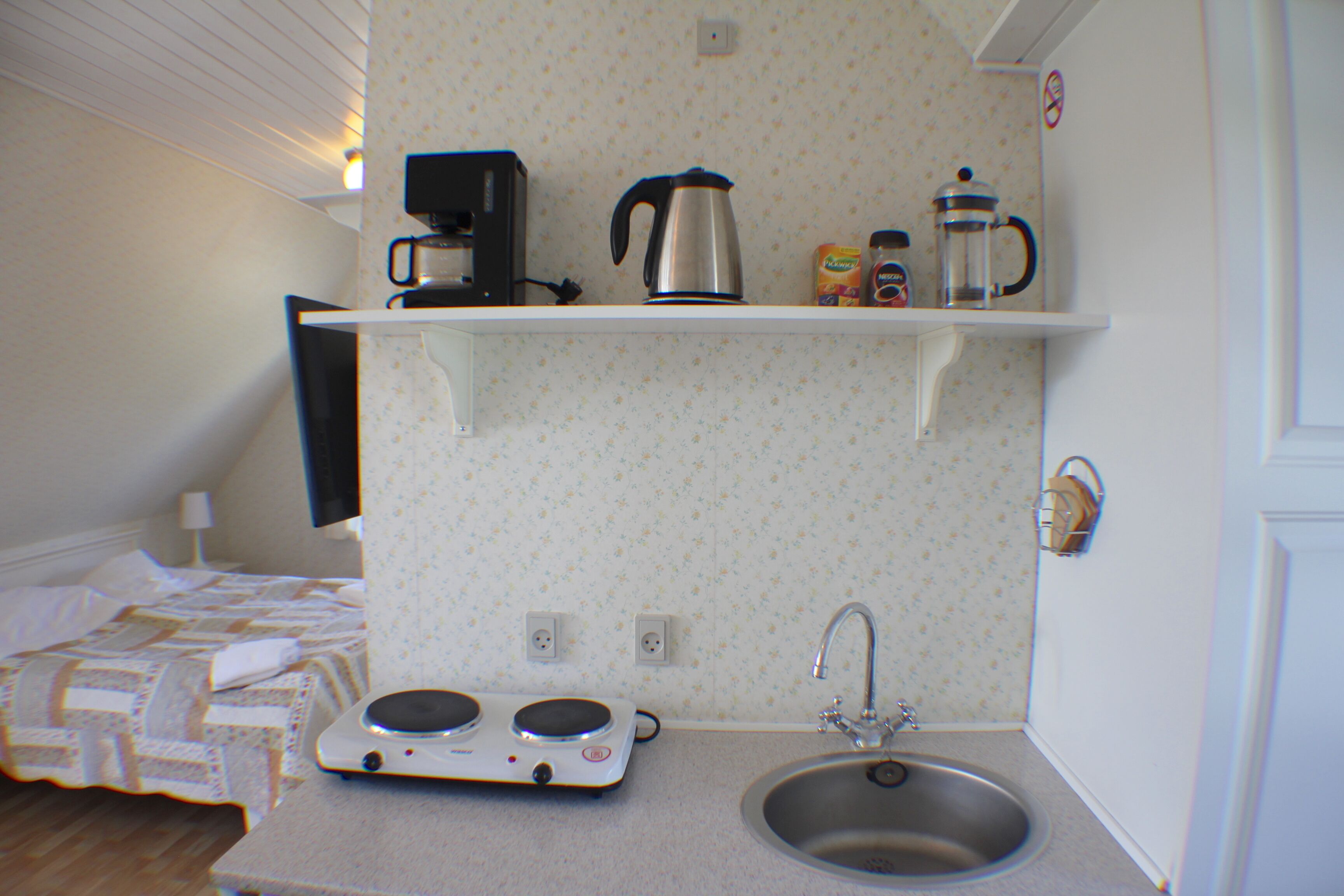 Una kitchenette compacta con cafetera, hervidor y un pequeño estante con condimentos.