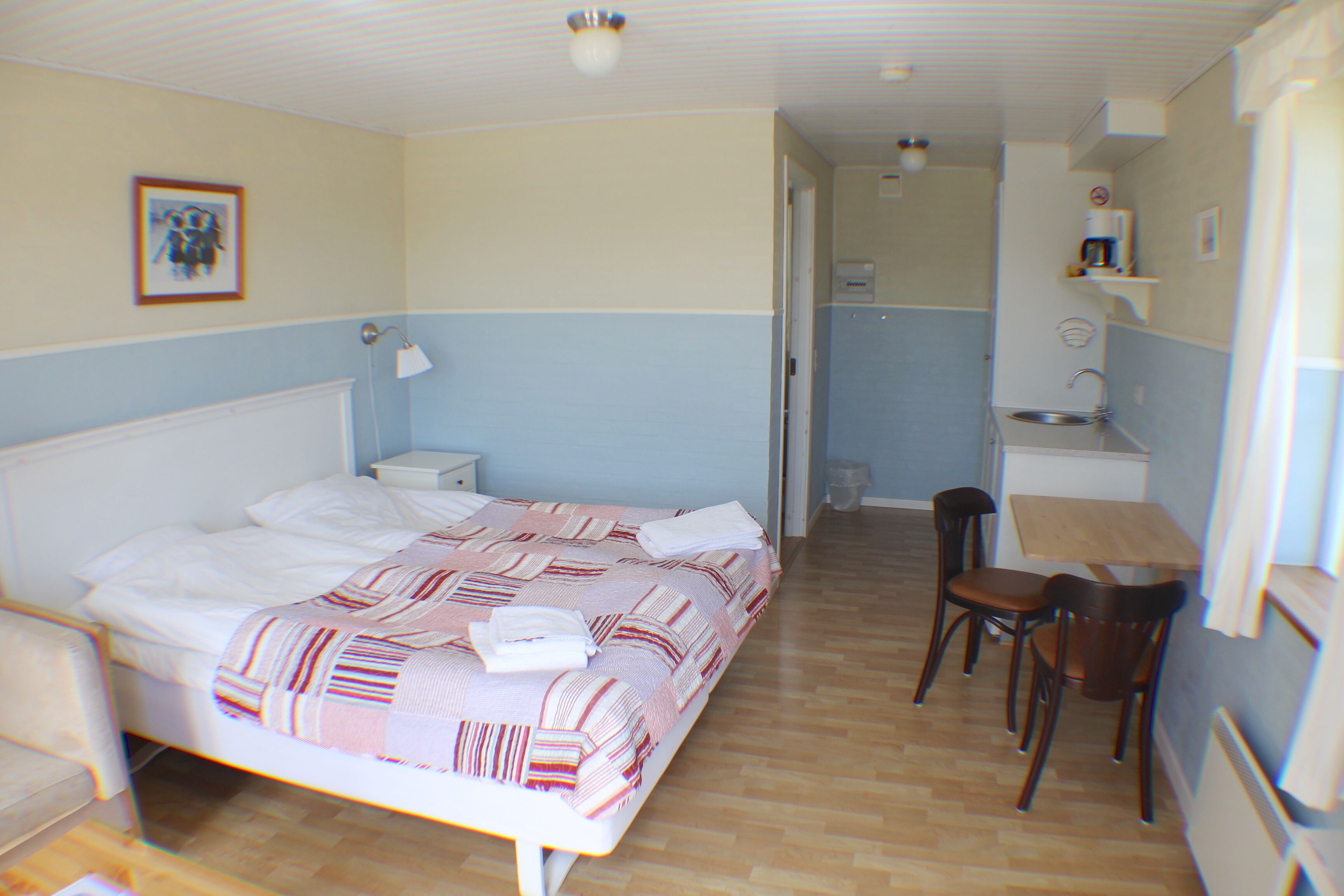 A bedroom with a bed, bedside table, and a desk with chairs.