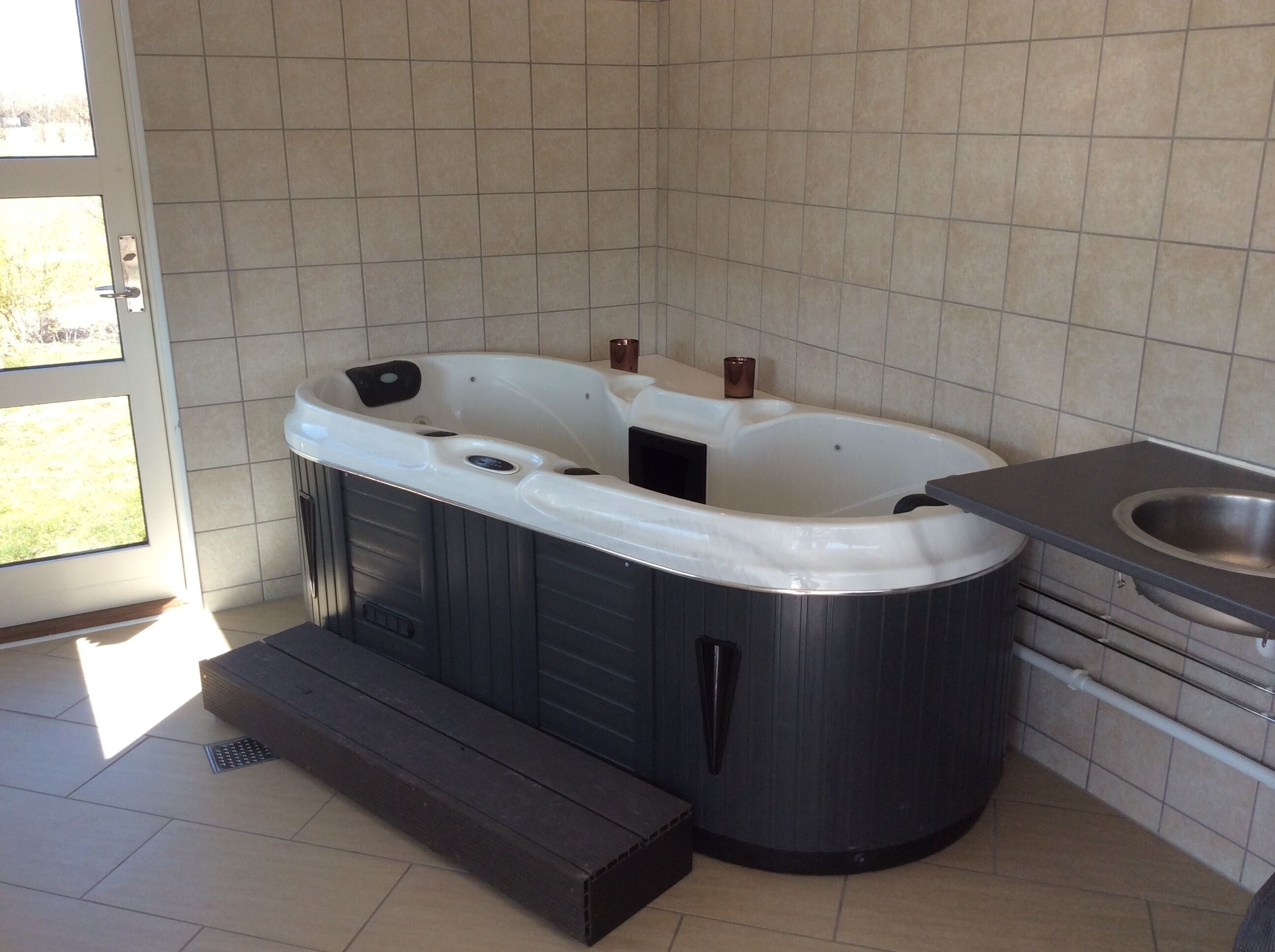 A hot tub in a bathroom with tiled walls and a window.