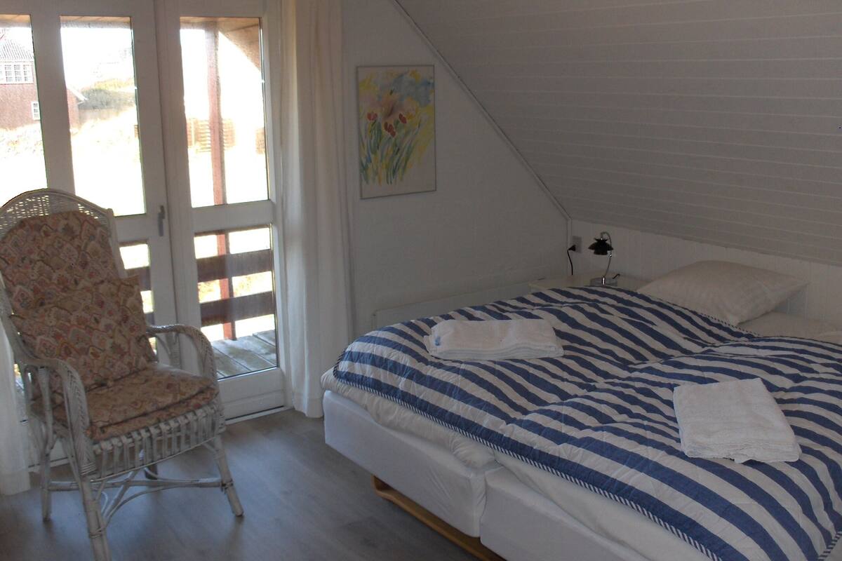 Ein Schlafzimmer mit einem Bett, einem Sessel, einem Fenster und einem Gemälde.