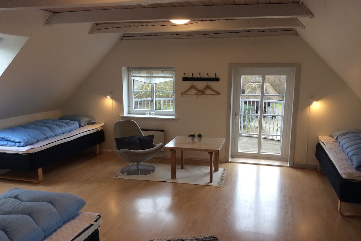 Ein gemütliches, helles Schlafzimmer im Dachgeschoss mit zwei Betten, einem Esstisch und einem Stuhl.