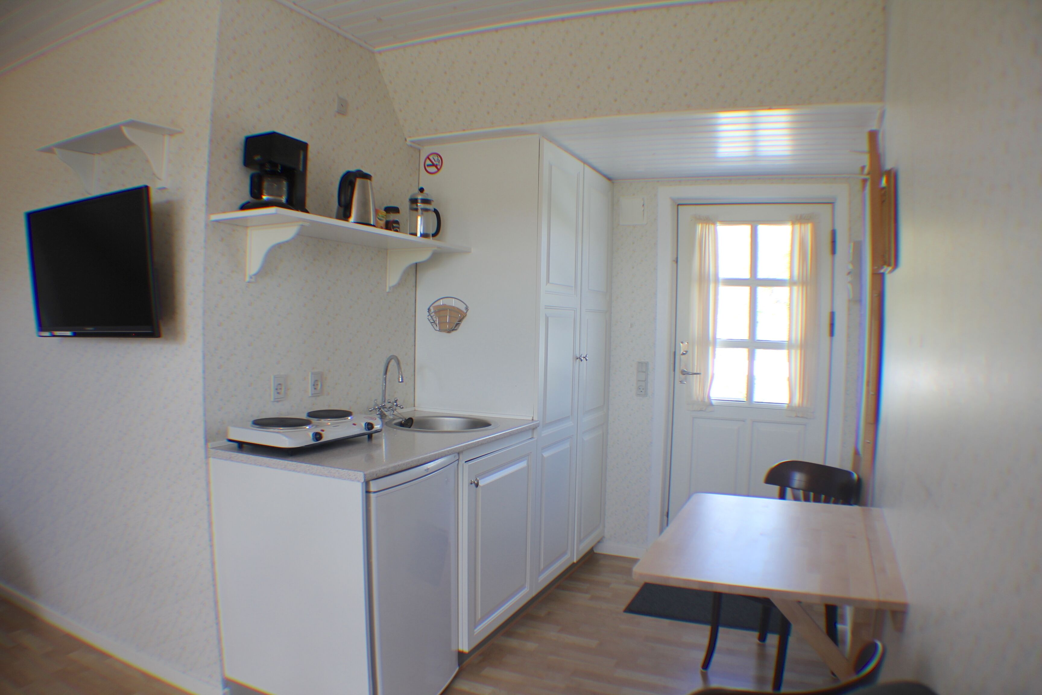 A compact kitchen with white cabinets, a sink, a coffee maker, and a small table.