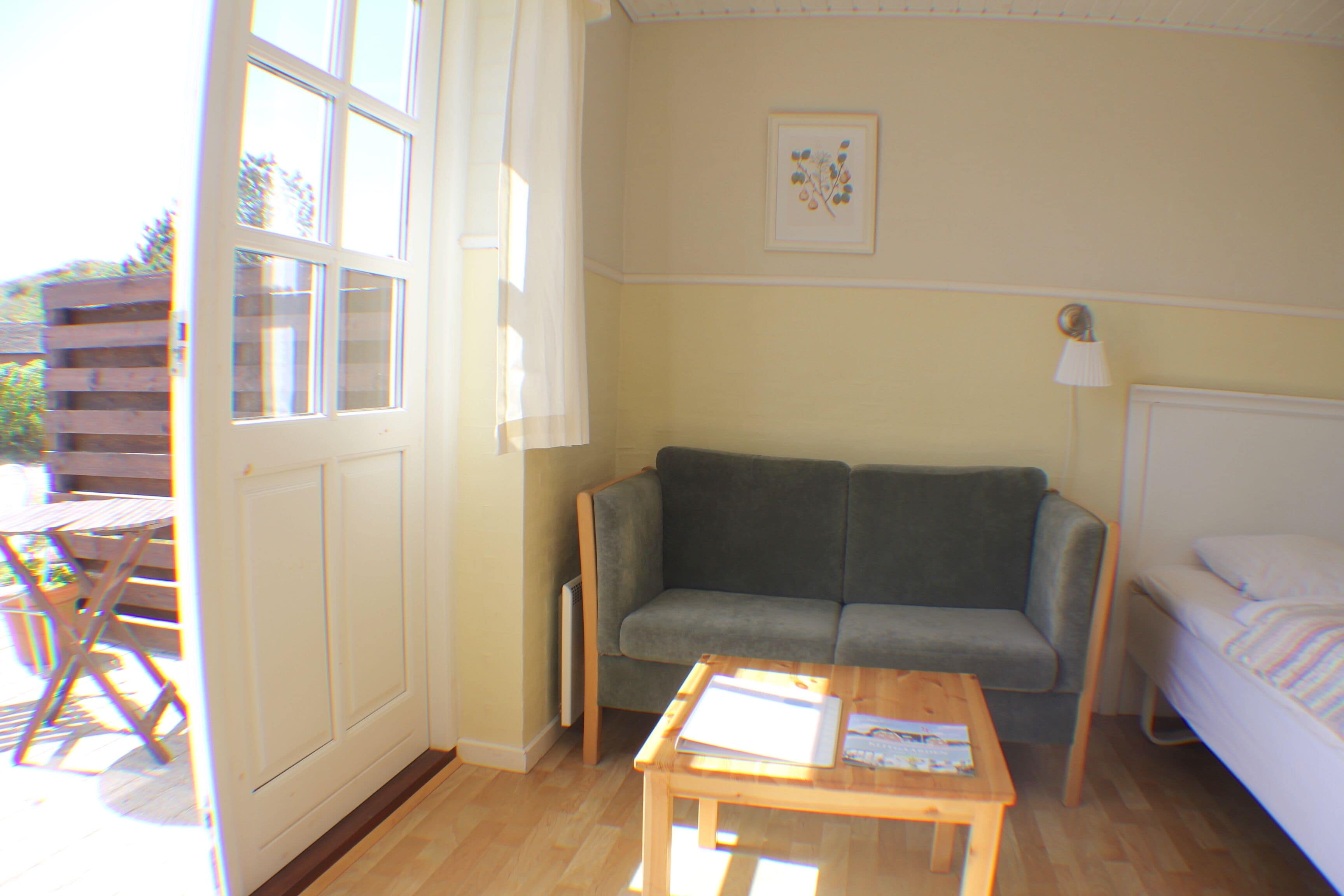 A room with a sofa, a bed, a wooden table, and a window with curtains.