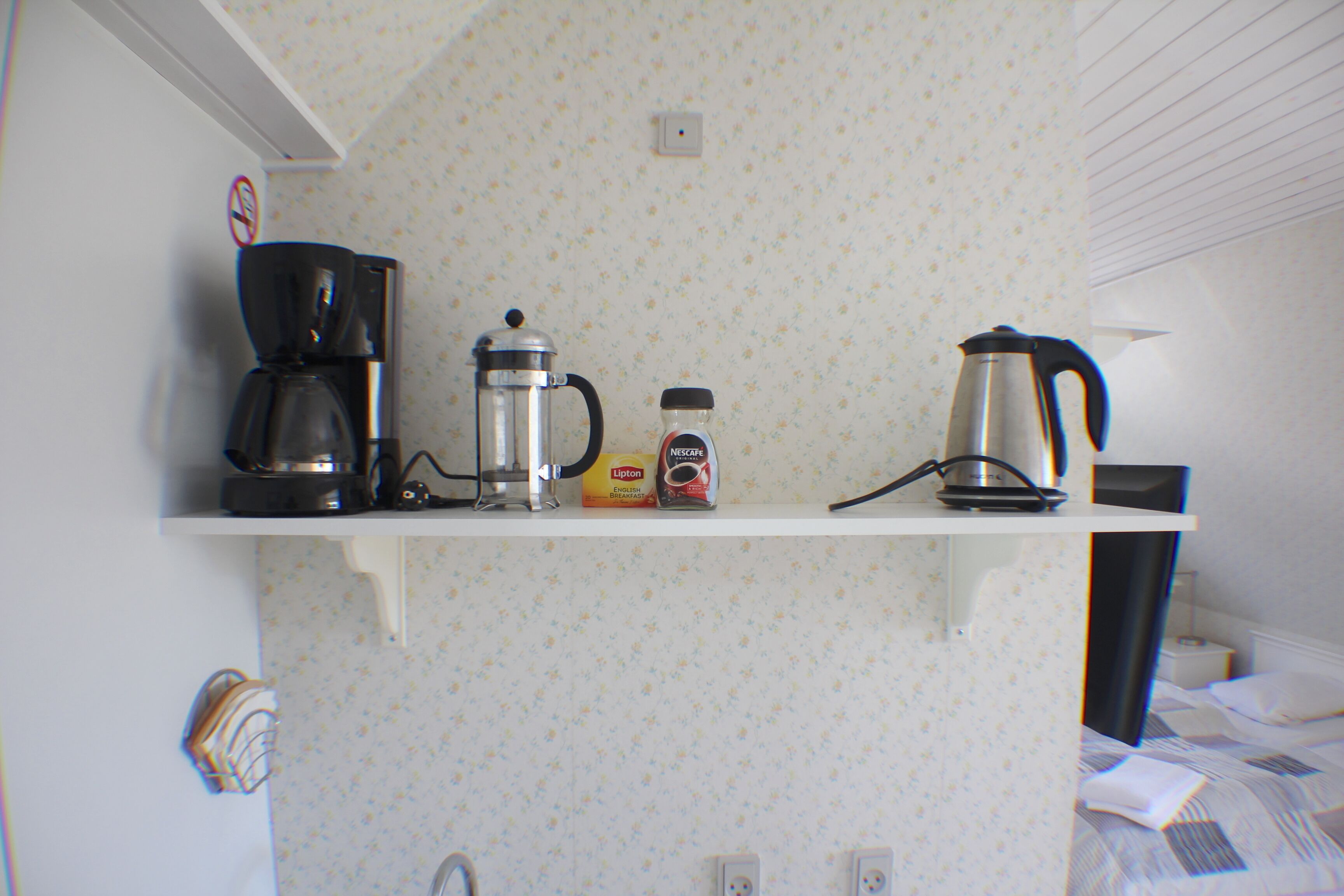 Een keuken met een koffiezetapparaat, een cafetière en een waterkoker op een witte plank.