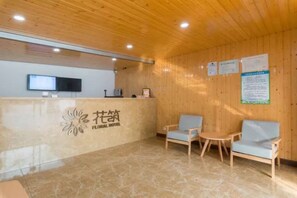 Zona de recepción con techo de madera, mostrador, televisor y dos sillas.