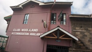 A pink building with a sign stating "CLUB WOODLAND ACCOMMODATION AVAILABLE". - Club Woodland (Matuu)