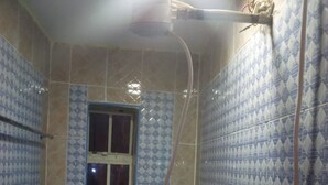 A small bathroom with patterned tiles, a window, a toilet, and a shower area. - Club Woodland (Matuu)