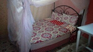 A single bed with a patterned bedspread, a canopy, and a bedside table. - Club Woodland (Matuu)