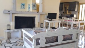 A living room with a fireplace, a television, and a dining area with chairs and a table. - Villa Sofia (Faistos)