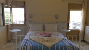 A bed with a white metal frame, two bedside tables, and a view of a balcony with a railing. - Villa Sofia (Faistos)