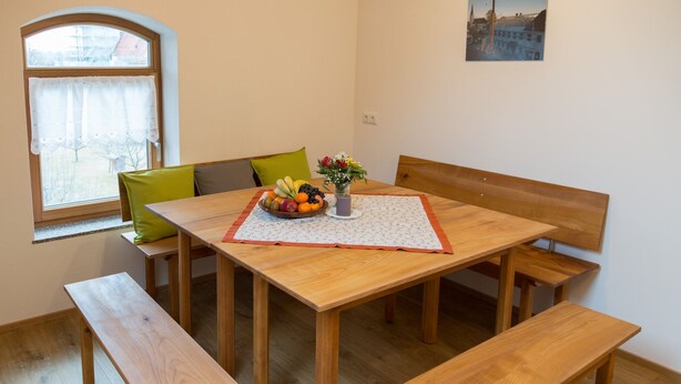A wooden dining table with benches, a fruit bowl, and a vase of flowers. - Pension Baumgartner (Rott a.Inn)