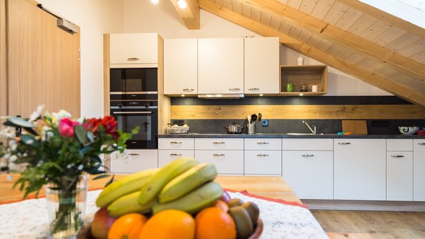 A modern kitchen with white cabinets, a built-in oven, and a wooden ceiling. - Pension Baumgartner (Rott a.Inn)