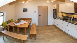 A compact kitchen with wooden cabinets, a dining table with benches, and a small window. - Pension Baumgartner (Rott a.Inn)