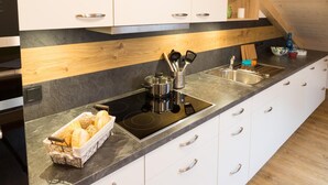A modern kitchen with a black countertop, white cabinets, and a wooden ceiling. - Pension Baumgartner (Rott a.Inn)