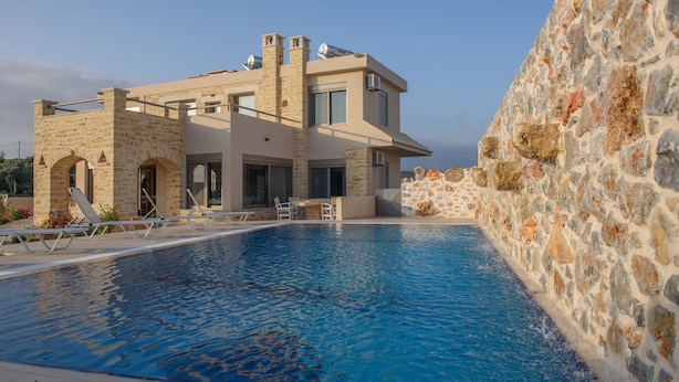 A modern house with a swimming pool, stone walls, and a clear sky. - Villa Xenophon (Faistos)