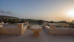 A stone bench on a rooftop terrace with a view of a hilly landscape and buildings in the distance. - Villa Xenophon (Faistos)