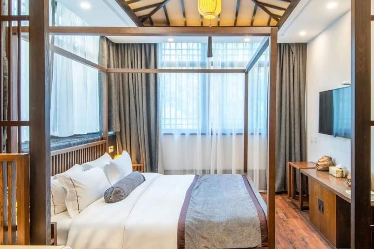A bedroom with a large bed, wooden floor, a desk with a TV, and a window with curtains.