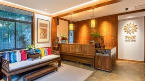 A reception area with a wooden bench, colorful cushions, a reception desk, and a wall with a decorative emblem. - Floral Hotel Aranya Resort Hangzhou (Hangzhou)