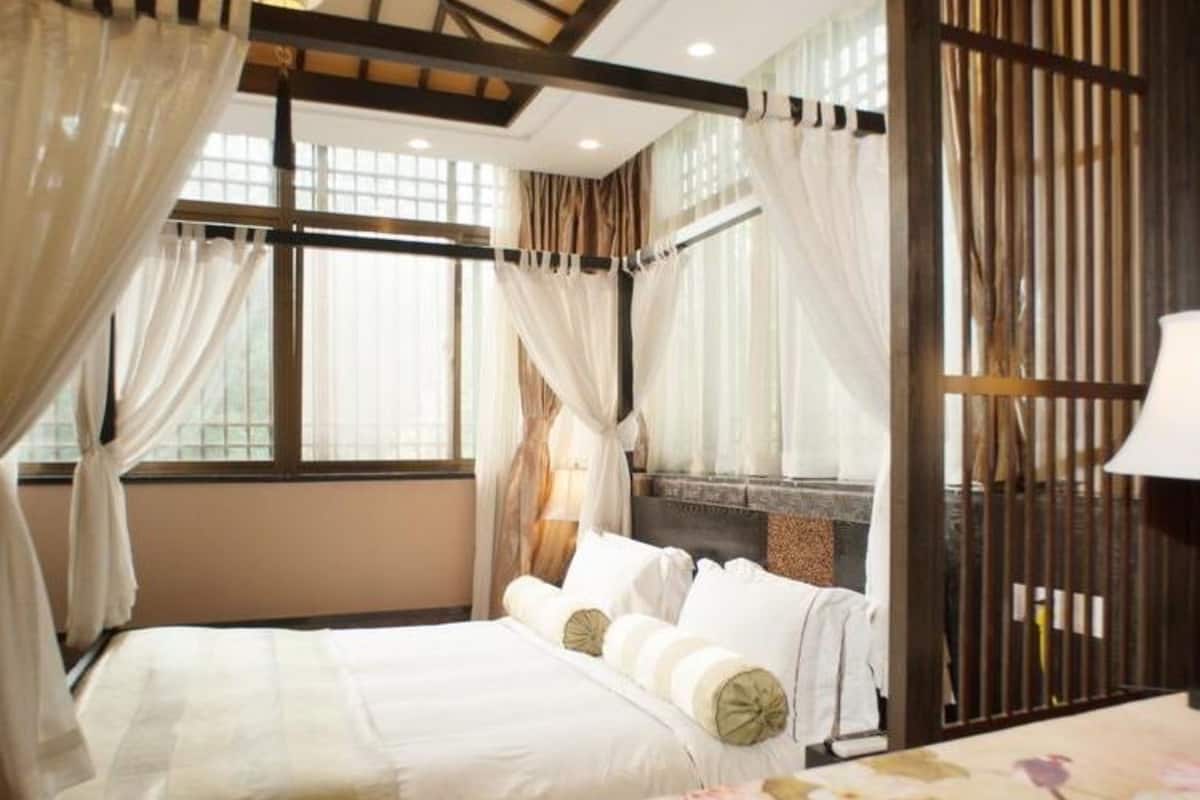 A hotel room with a bed, a bedside table, and a window with curtains.