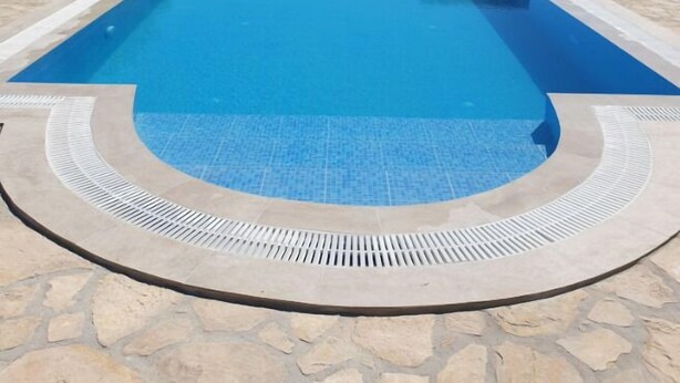 A rectangular swimming pool with a stone border and a tiled edge, surrounded by a stone wall and vegetation. - Villa Efthalia (Faistos)