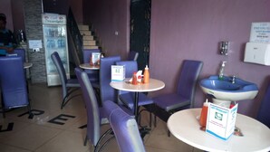 A cafe with purple chairs and tables, a refrigerator, and a sign for guest rooms. - Dream Light Hotel (Matuu)