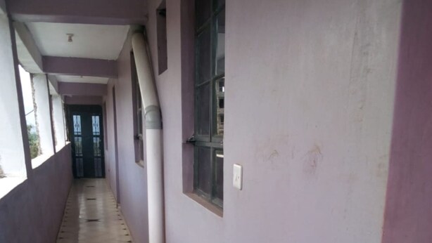 A corridor with tiled flooring, a window with a metal grille, and a door at the end. - Dream Light Hotel (Matuu)