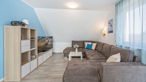 A modern living room with a sectional sofa, a TV on a stand, a wooden cabinet, and a small table. - Modern vacation apartment in Loddin with garden, WLAN & playground - quiet and on the beach (Loddin)