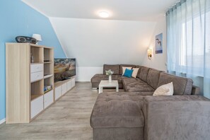 A modern living room with a sectional sofa, a TV on a stand, a wooden cabinet, and a small table. - Modern vacation apartment in Loddin with garden, WLAN & playground - quiet and on the beach (Loddin)