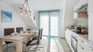 A modern kitchen with a dining area, featuring a wooden table, chairs, and a hanging light fixture. - Modern vacation apartment in Loddin with garden, WLAN & playground - quiet and on the beach (Loddin)