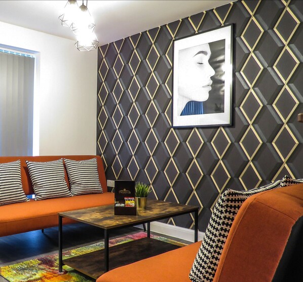 Un salon moderne avec un mur orné d’un motif géométrique, une œuvre d’art encadrée, un canapé, une table basse et une plante en pot.