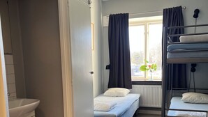 Une petite pièce comprenant un lit superposé, un lit simple, une fenêtre avec des rideaux, un radiateur et un lavabo.