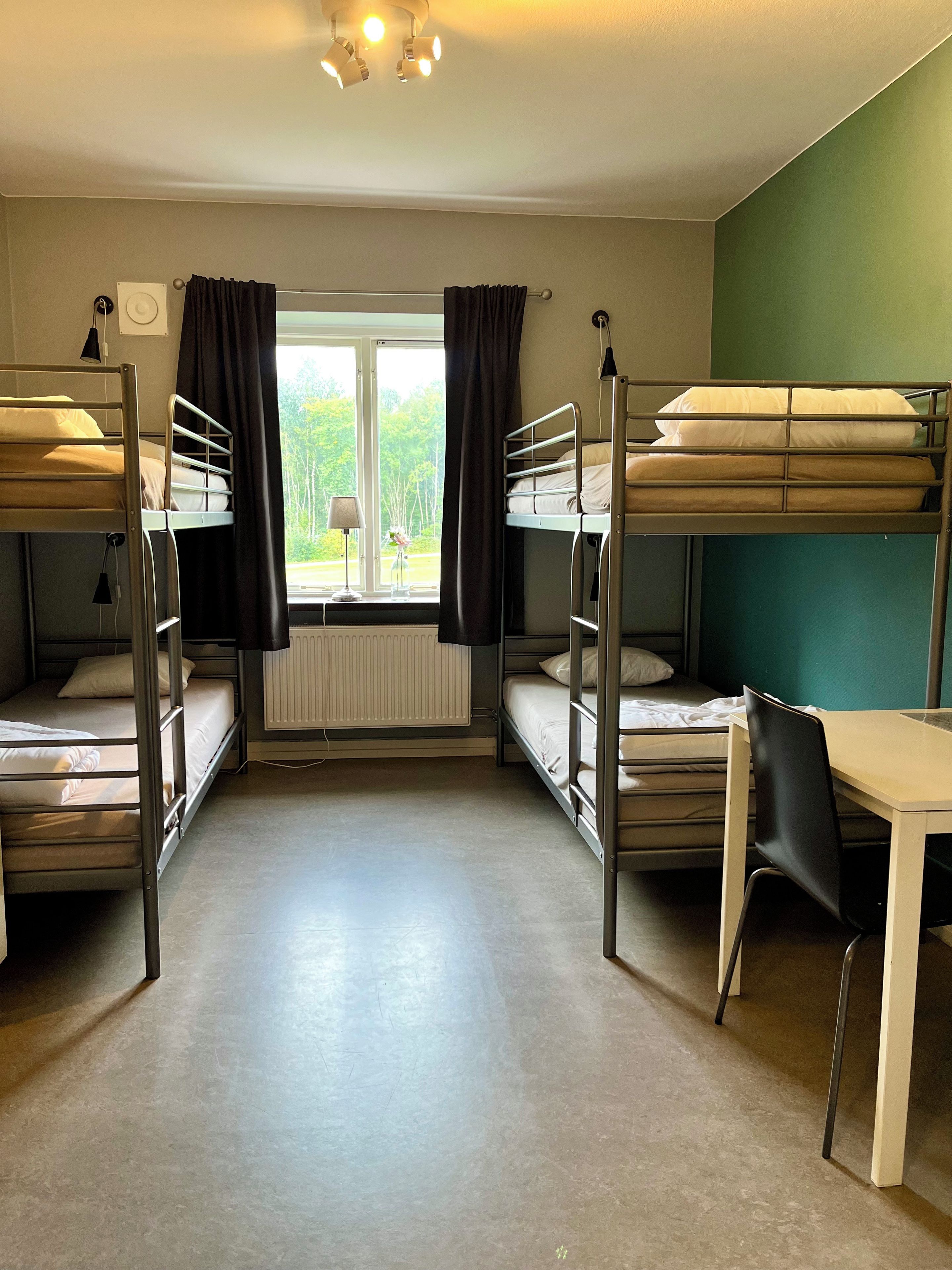 Une chambre de dortoir avec des lits superposés, une table et une fenêtre avec des rideaux.