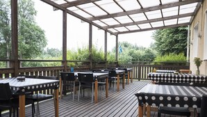 Eine Terrasse im Freien mit Tischen und Stühlen, ein Holzdeck und ein überdachter Bereich mit Blick auf Grünflächen.