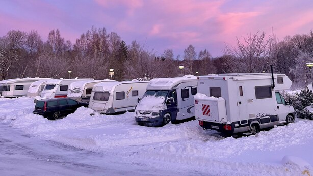 Eine Reihe von Wohnmobilen steht in einem verschneiten Parkplatz, der bewölkt ist.