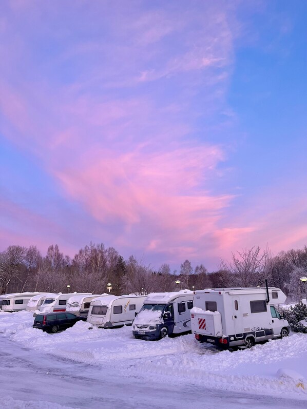 Une rangée de camping-cars est stationnée sur un parking enneigé, sous un ciel dégagé.