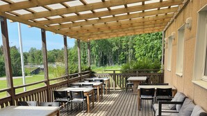 Une terrasse extérieure avec des tables et des chaises en bois, une plateforme en bois et une structure en forme de pergola.