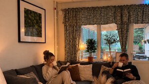 Ein gemütliches Wohnzimmer mit einer Eckcouch, einem Couchtisch mit Kerzen und einem großen Fenster mit Vorhängen.