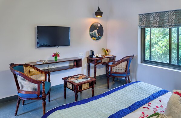 Una habitación con una cama, dos sillas de madera, una mesita, televisión y una ventana con vista a zonas verdes.