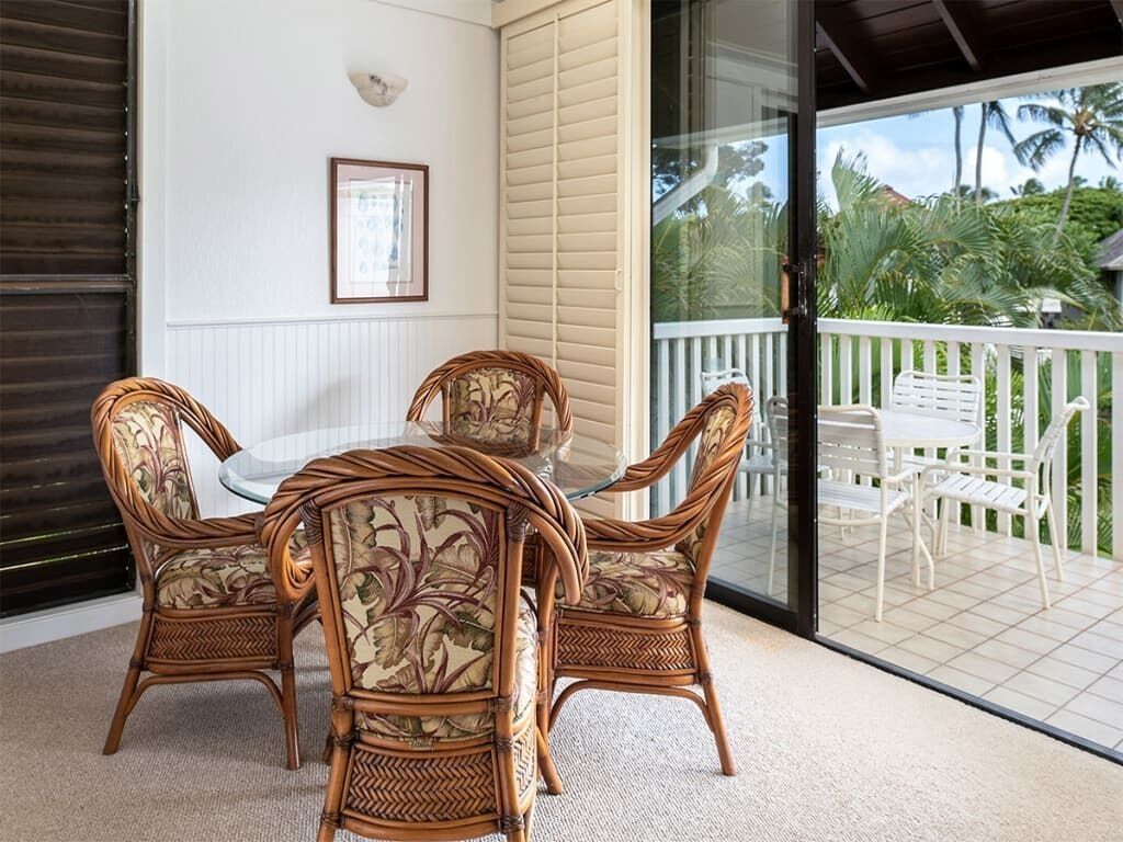 Ein Balkon mit Korbmöbeln, einem gerahmten Bild an der Wand und Blick auf Palmen.